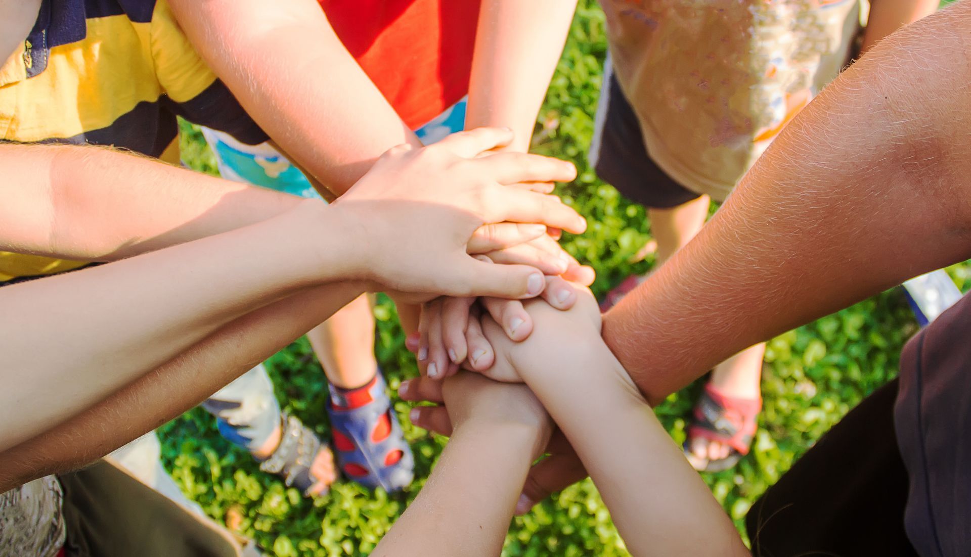 Hands of several people stacked together in a team huddle, in front of grass.