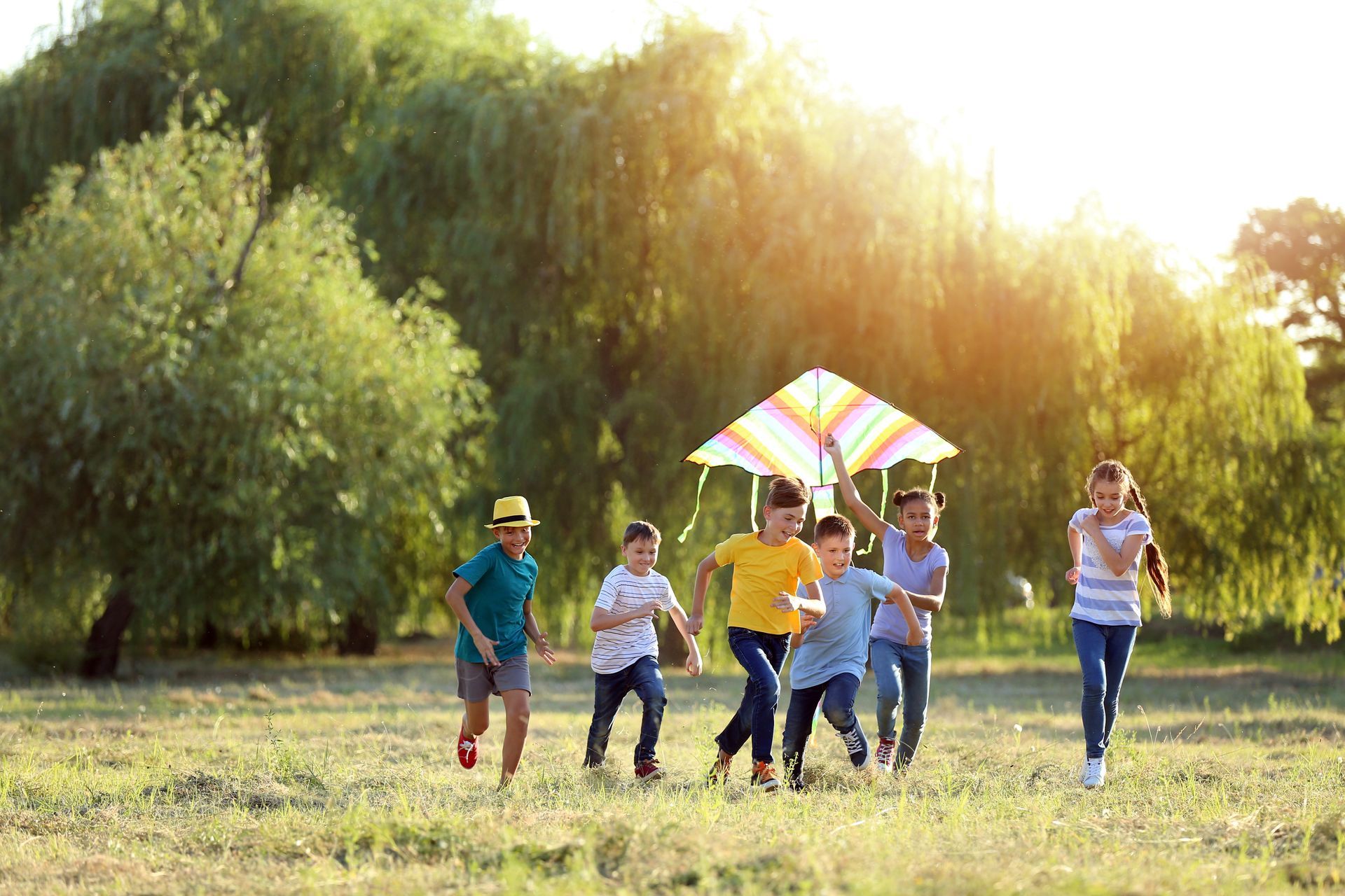 Children running in a grassy field, holding and flying a colorful kite.
