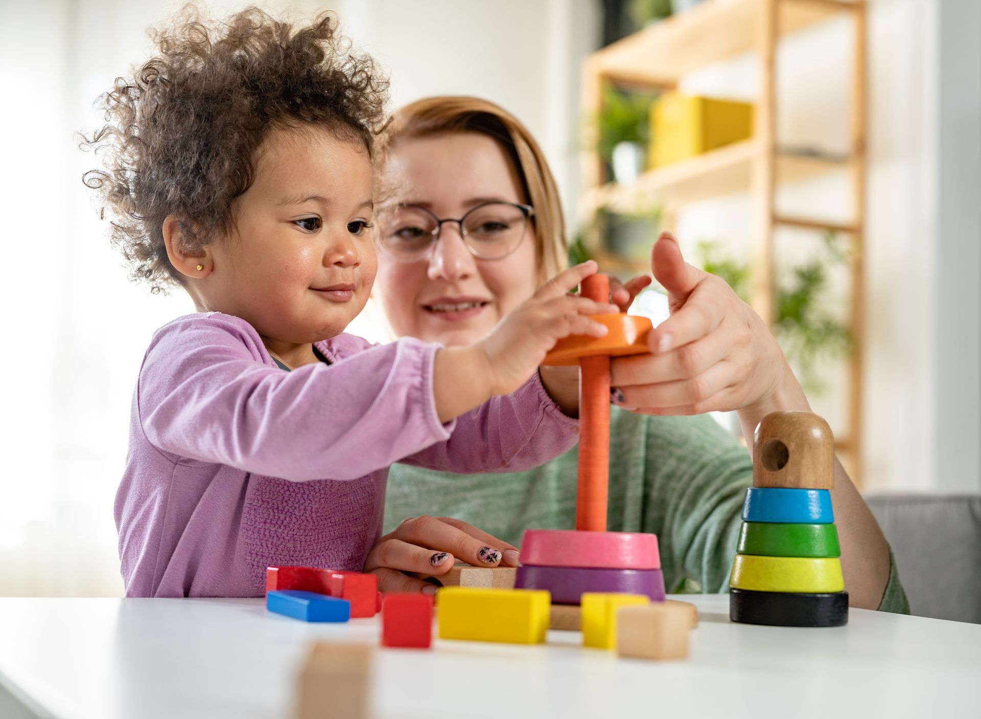 Child and adult playing with wooden stacking toy at a table.