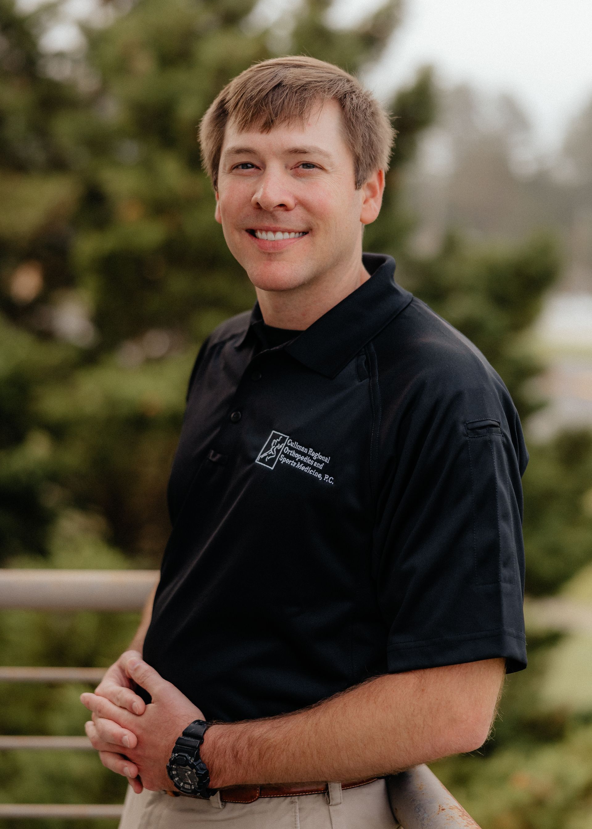 Patrick Harbison, CRNP in a black shirt and khaki pants is standing next to a railing.