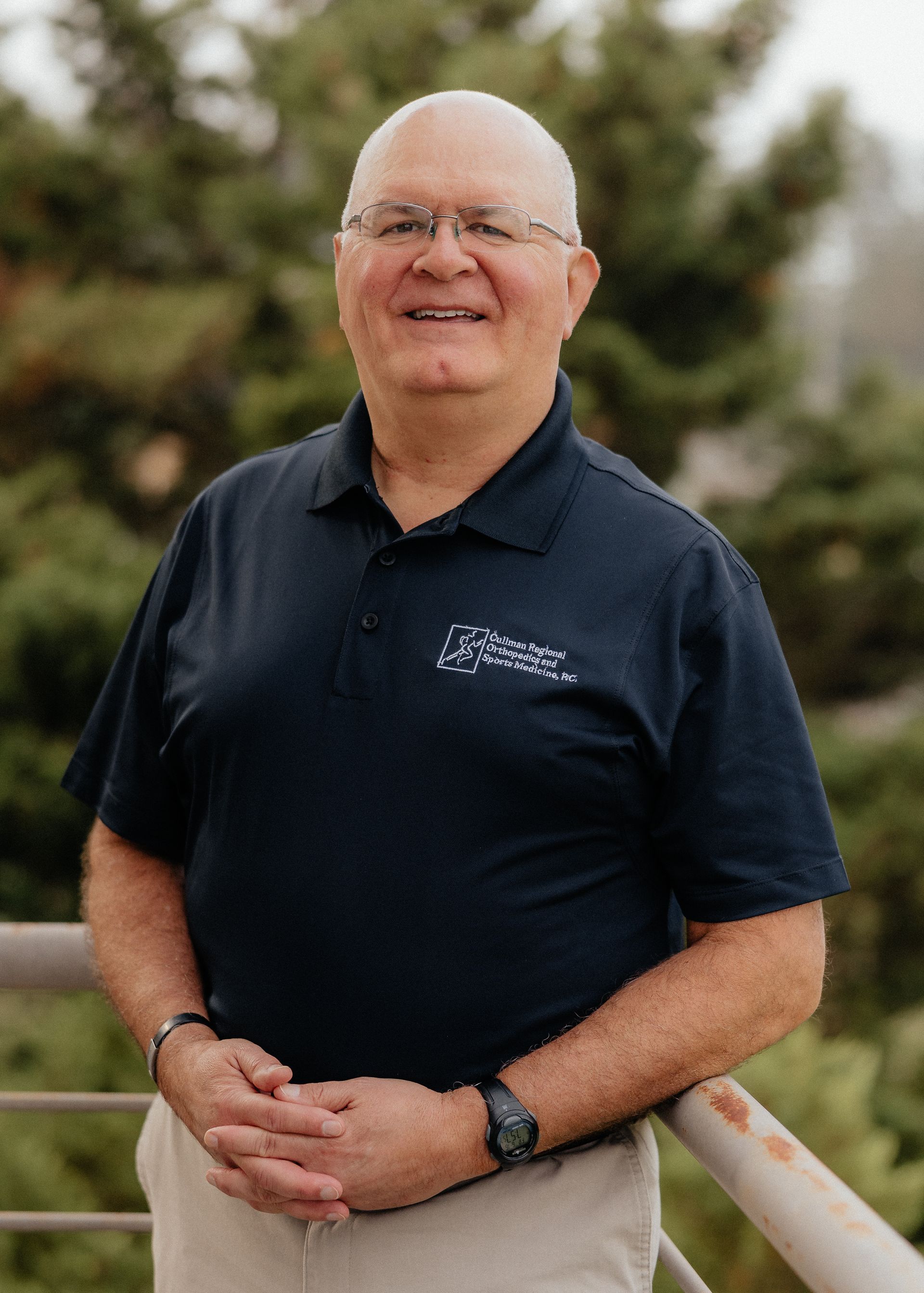 Dr. Ben Gomez in a blue shirt is standing with his arms crossed and smiling.
