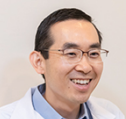 Smiling Asian man in glasses and a white coat.