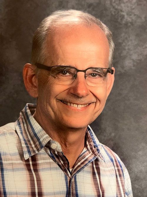 Smiling older man wearing glasses and a plaid shirt, posing for a photo.