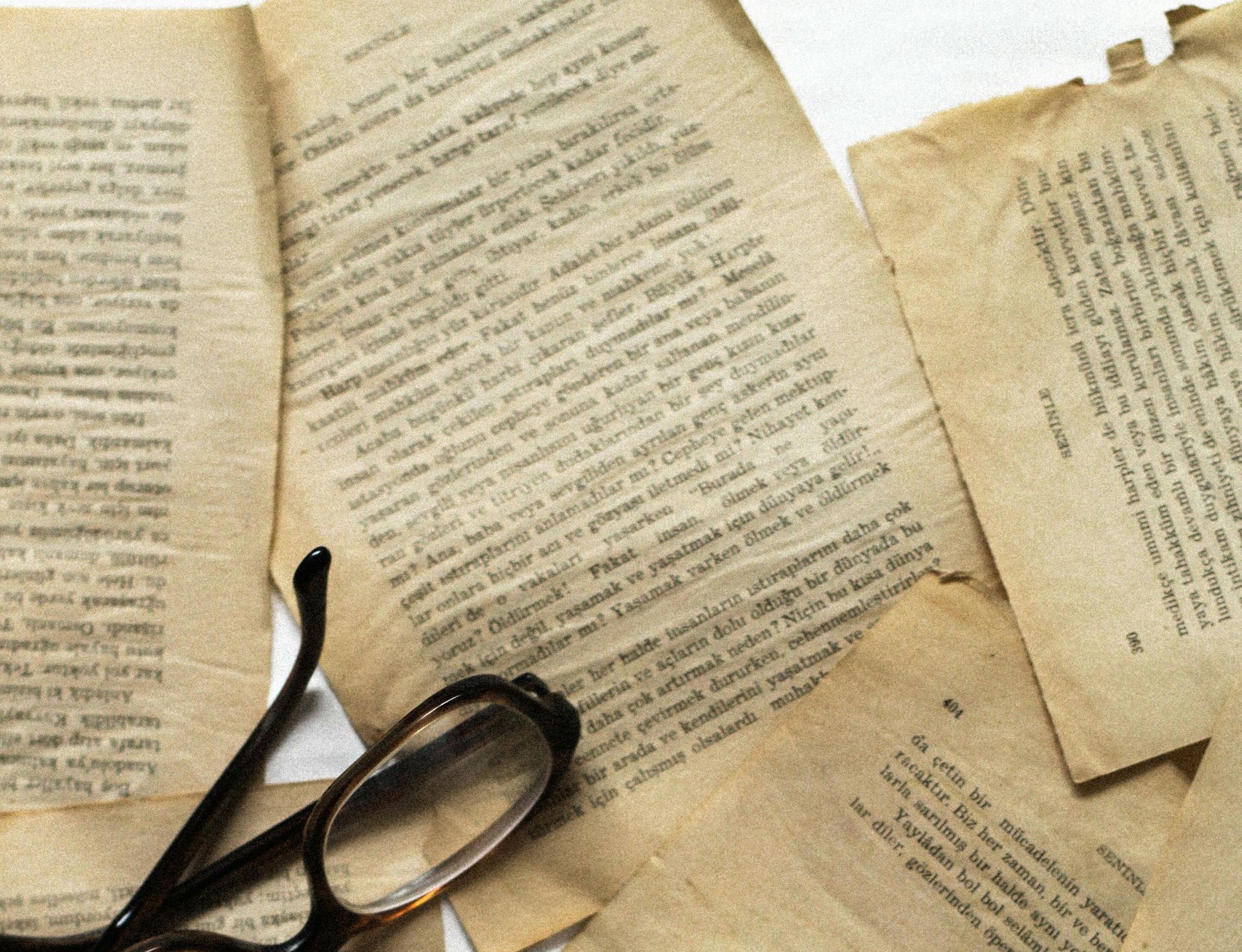 Close-up of old papers with handwritten text, scattered with reading glasses. Beige and sepia tones.