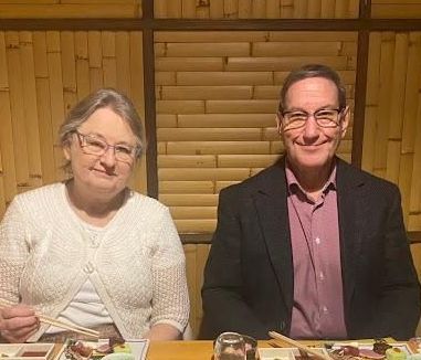Two people, a woman and a man, at a table. They are eating with chopsticks. The background is bamboo.