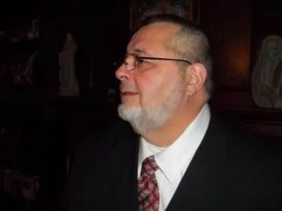 A man with a beard and glasses is wearing a suit and tie.