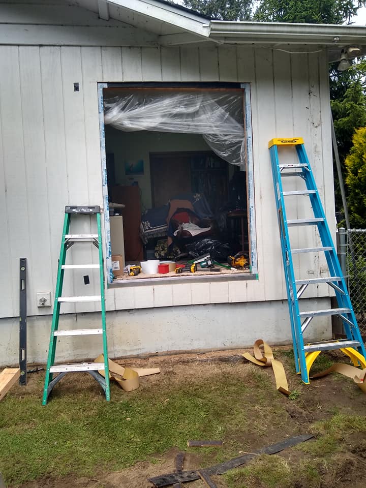 Two ladders are sitting in front of a window on the side of a house.