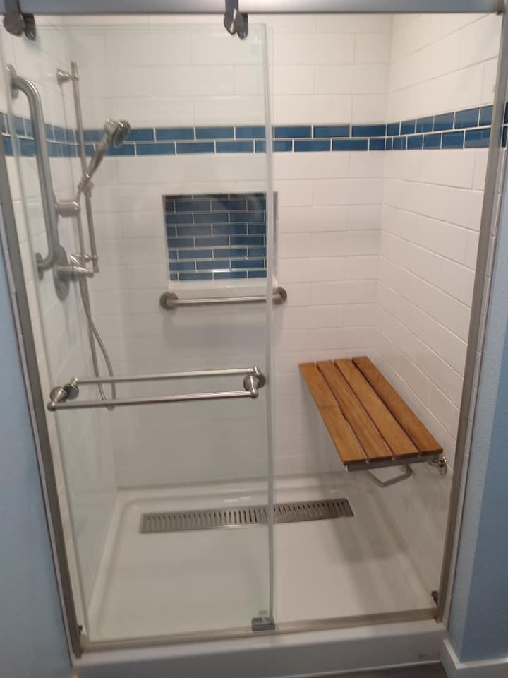 A shower with a wooden bench in it and a sliding glass door.