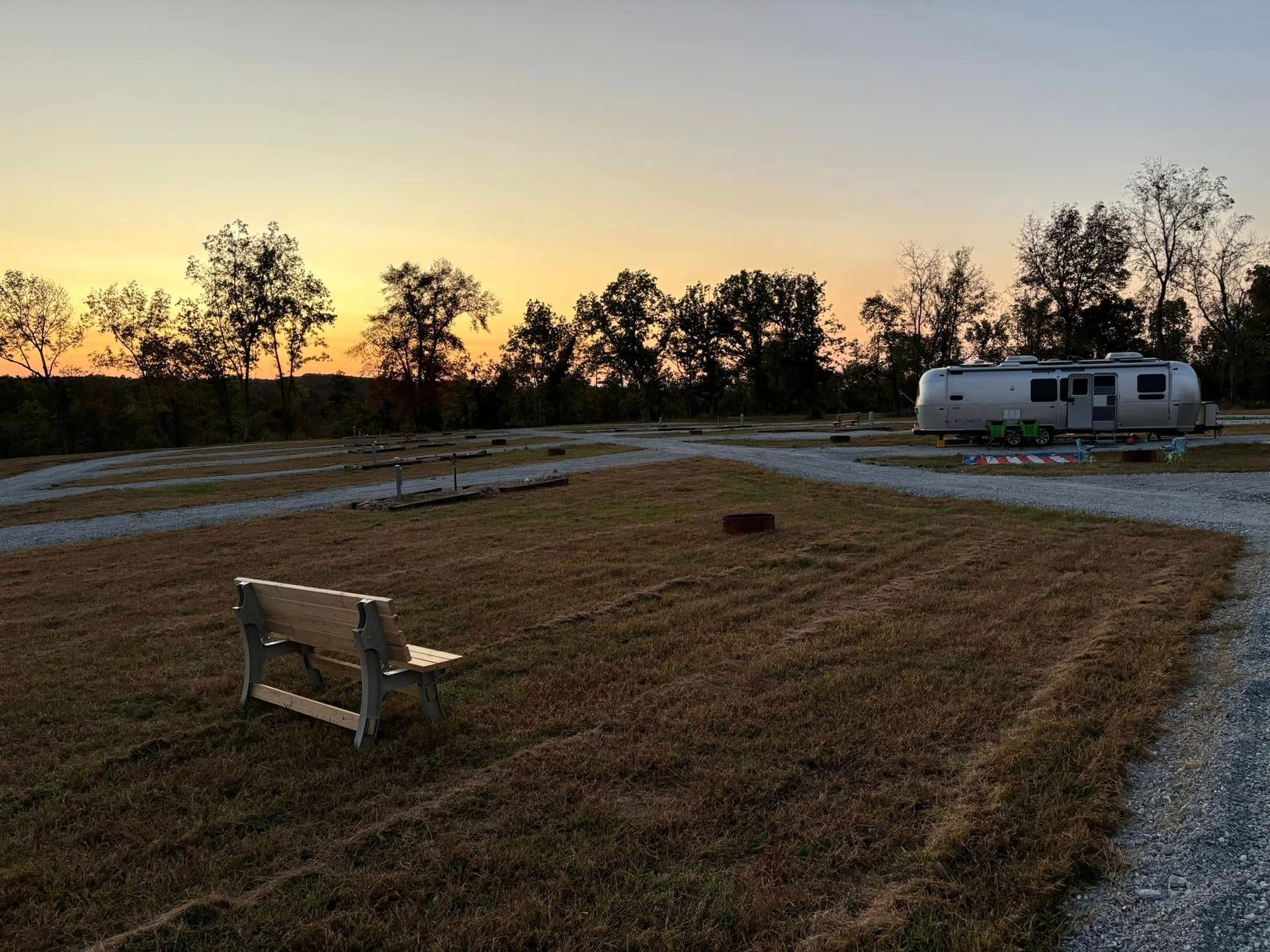 A park bench is sitting in the middle of a field with a rv parked in the background.