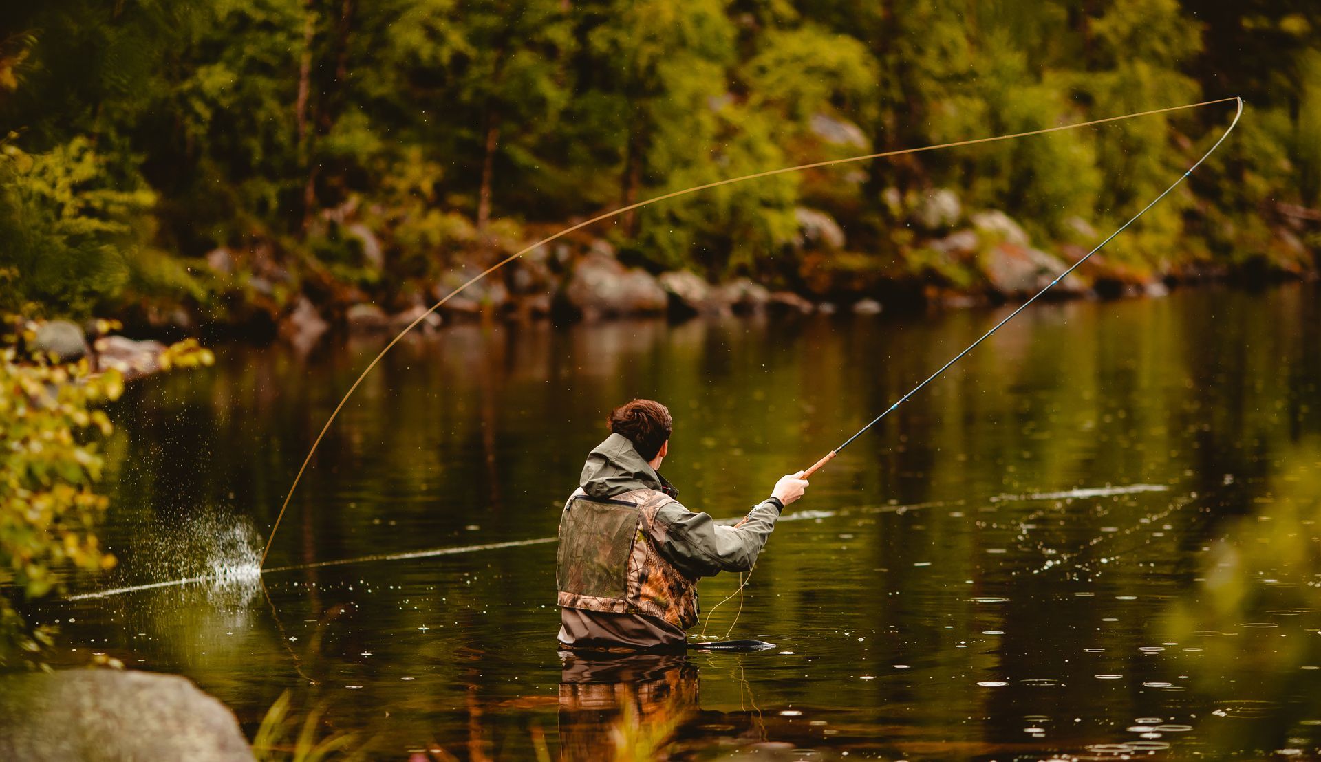 A man is fishing in a river with a fishing rod.