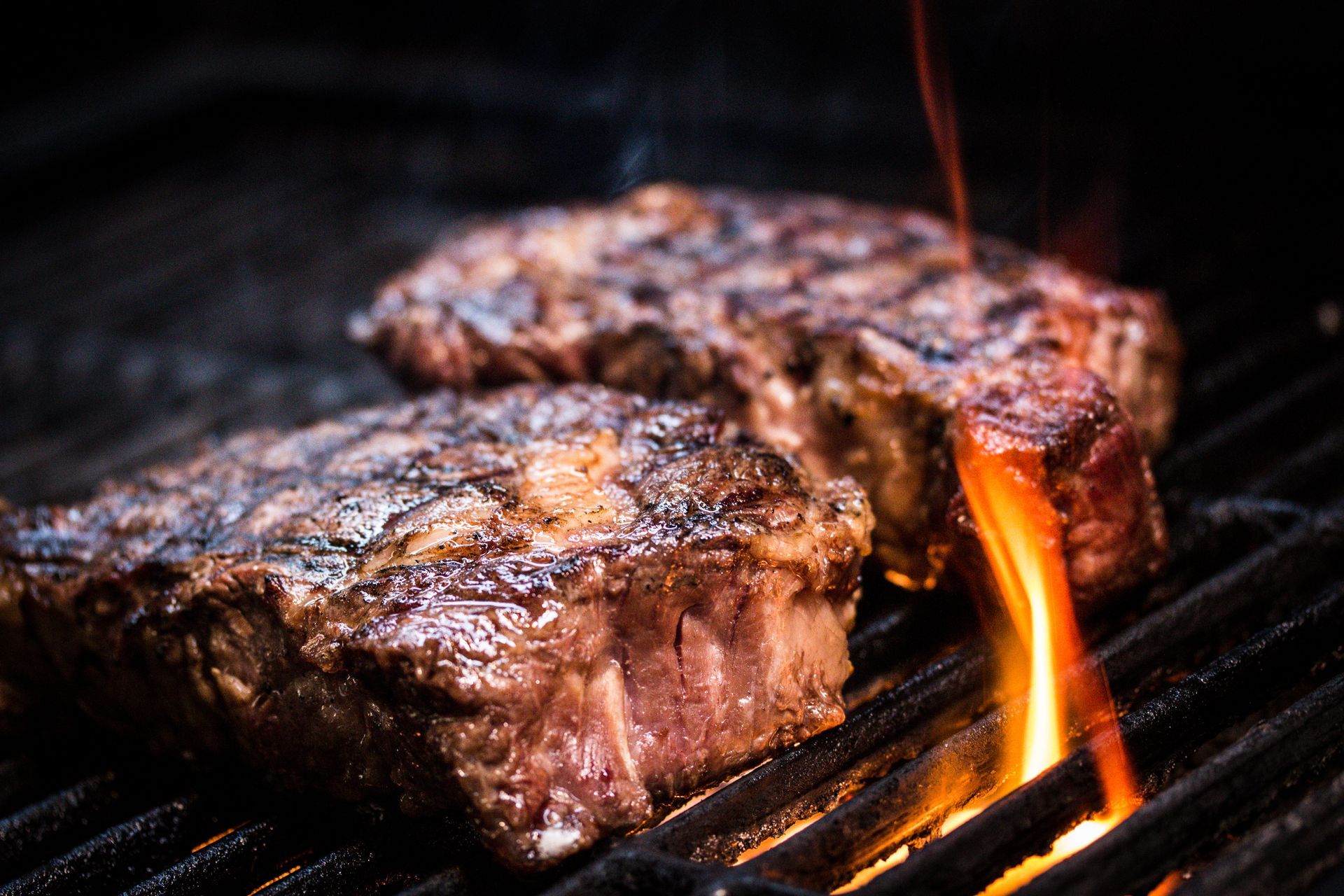 Two steaks are cooking on a grill with flames coming out of them.