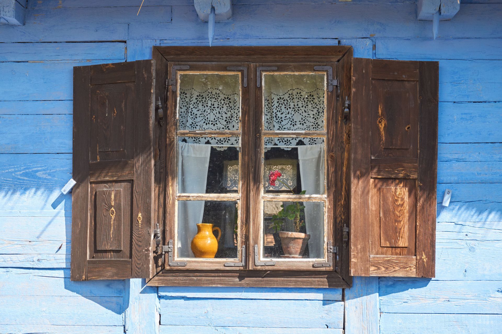 A blue wooden house with a window with shutters open and a vase in the window.