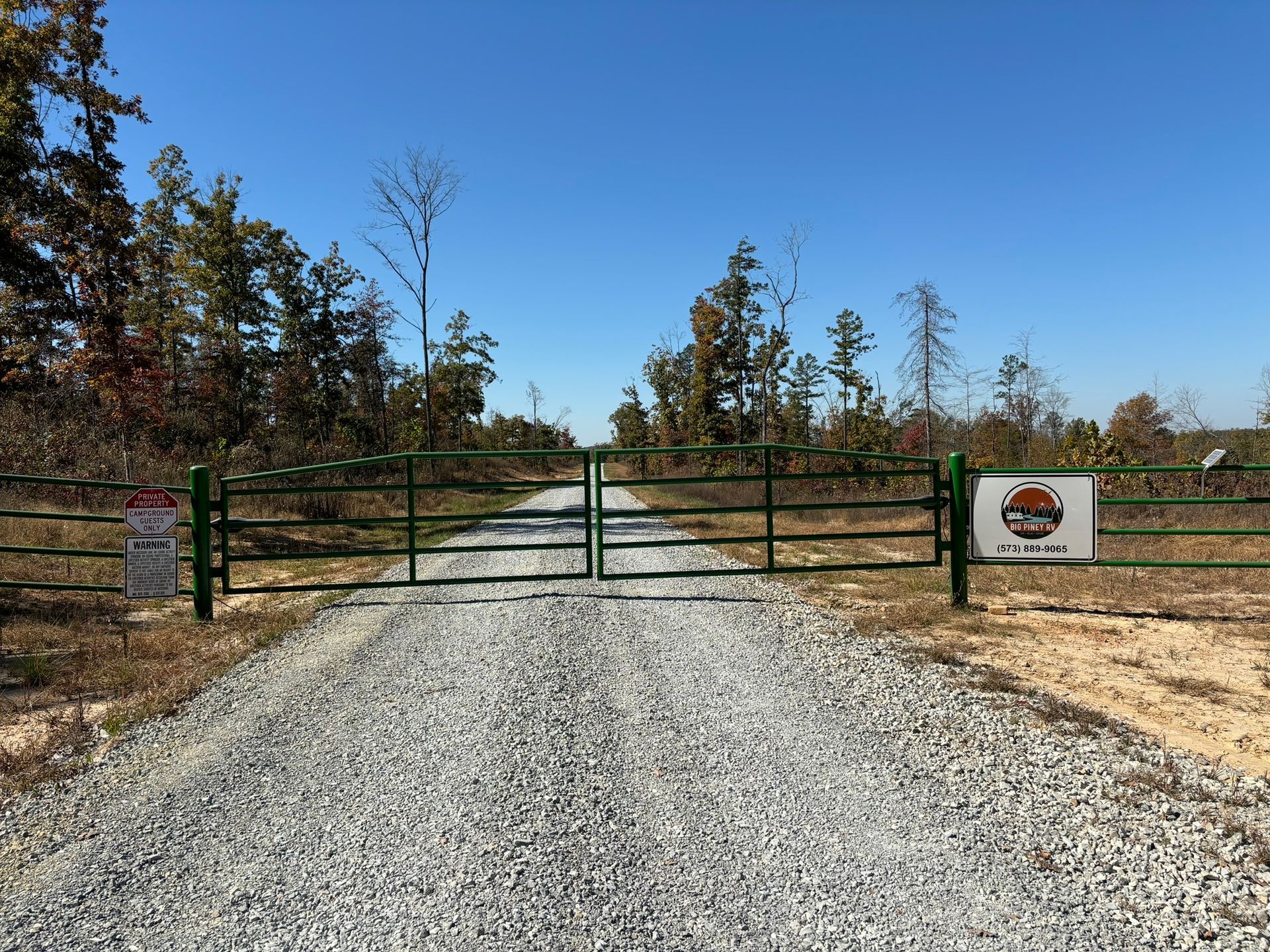 A gravel road with a green gate on the side of it
