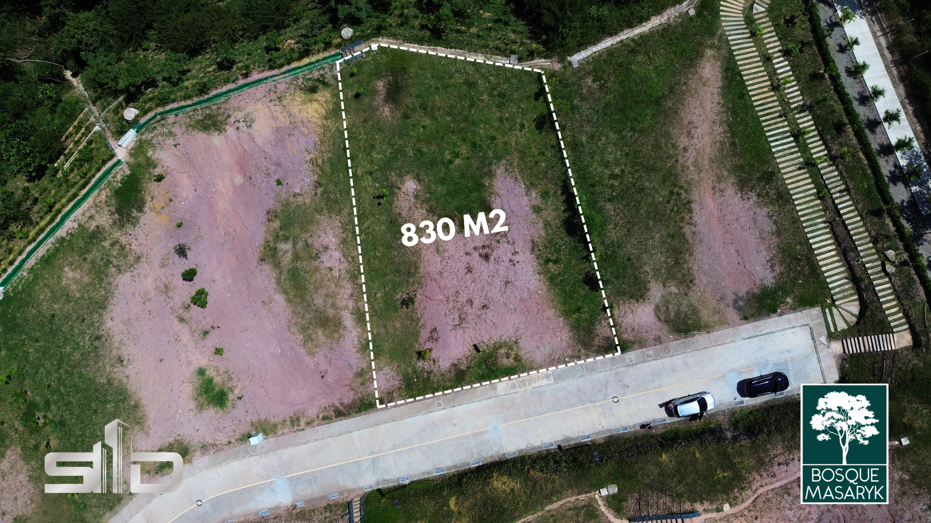 Una vista aérea muestra una parcela de terreno de 830 metros cuadrados delimitada por líneas discontinuas blancas, junto a una carretera pavimentada y una zona de aparcamiento.
