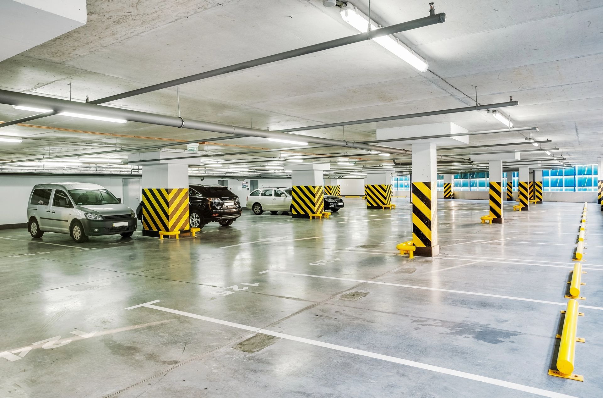 Aparcamiento subterráneo con coches aparcados en plazas señalizadas, columnas con franjas amarillas y negras.