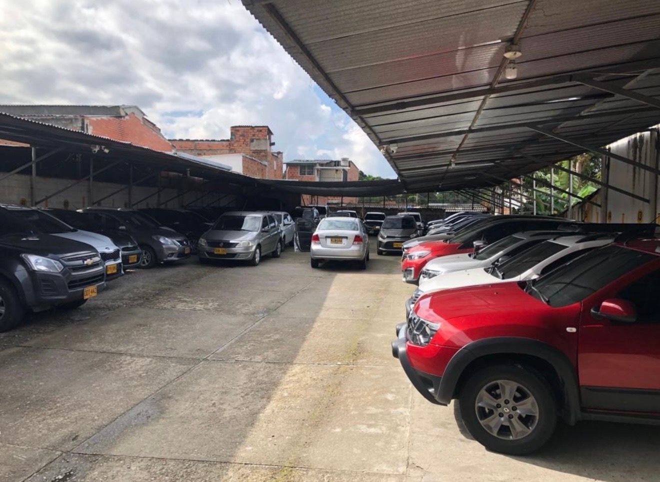 Aparcamiento subterráneo con coches aparcados, columnas con rayas negras y amarillas y luces fluorescentes en el techo.