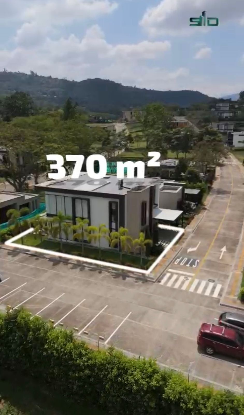 Paisaje urbano con edificios de ladrillo y blanco, árboles verdes y montañas al fondo bajo un cielo nublado.