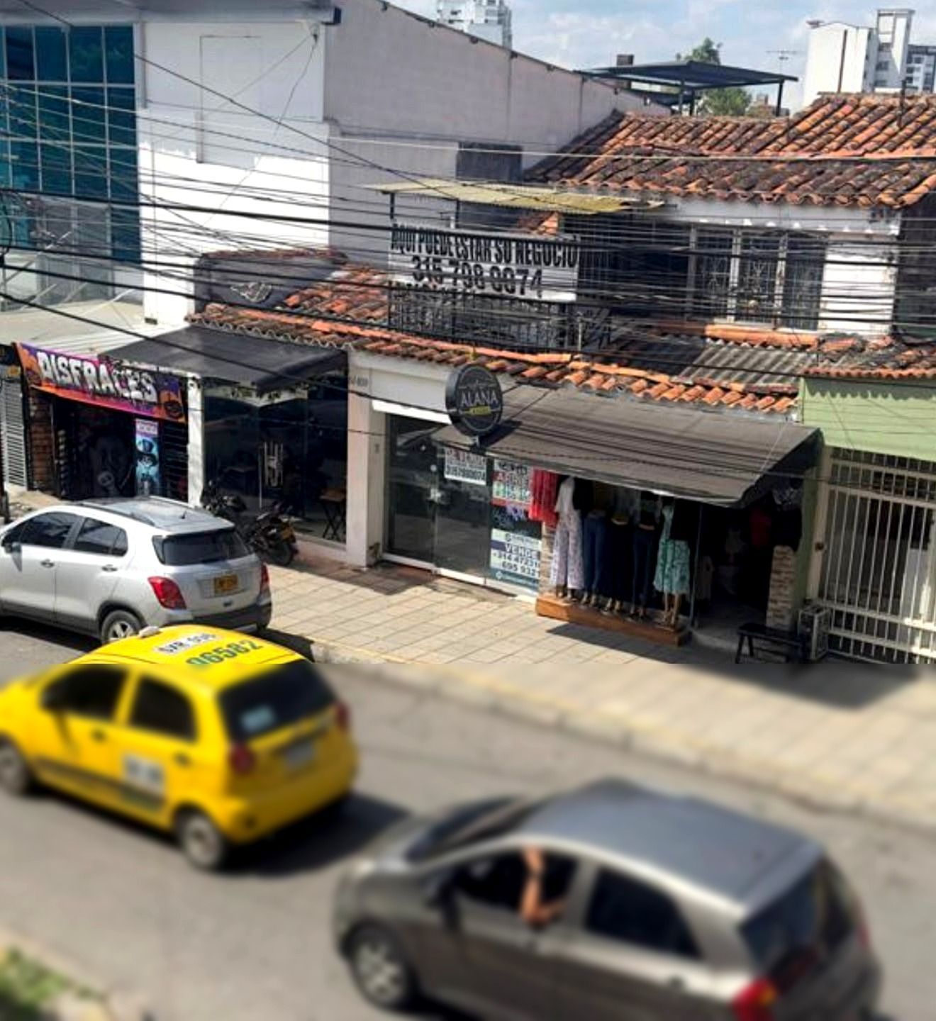 Exterior de casa moderna con amplios ventanales, patio y vista parcial a una cancha de tenis, bajo un cielo nublado.