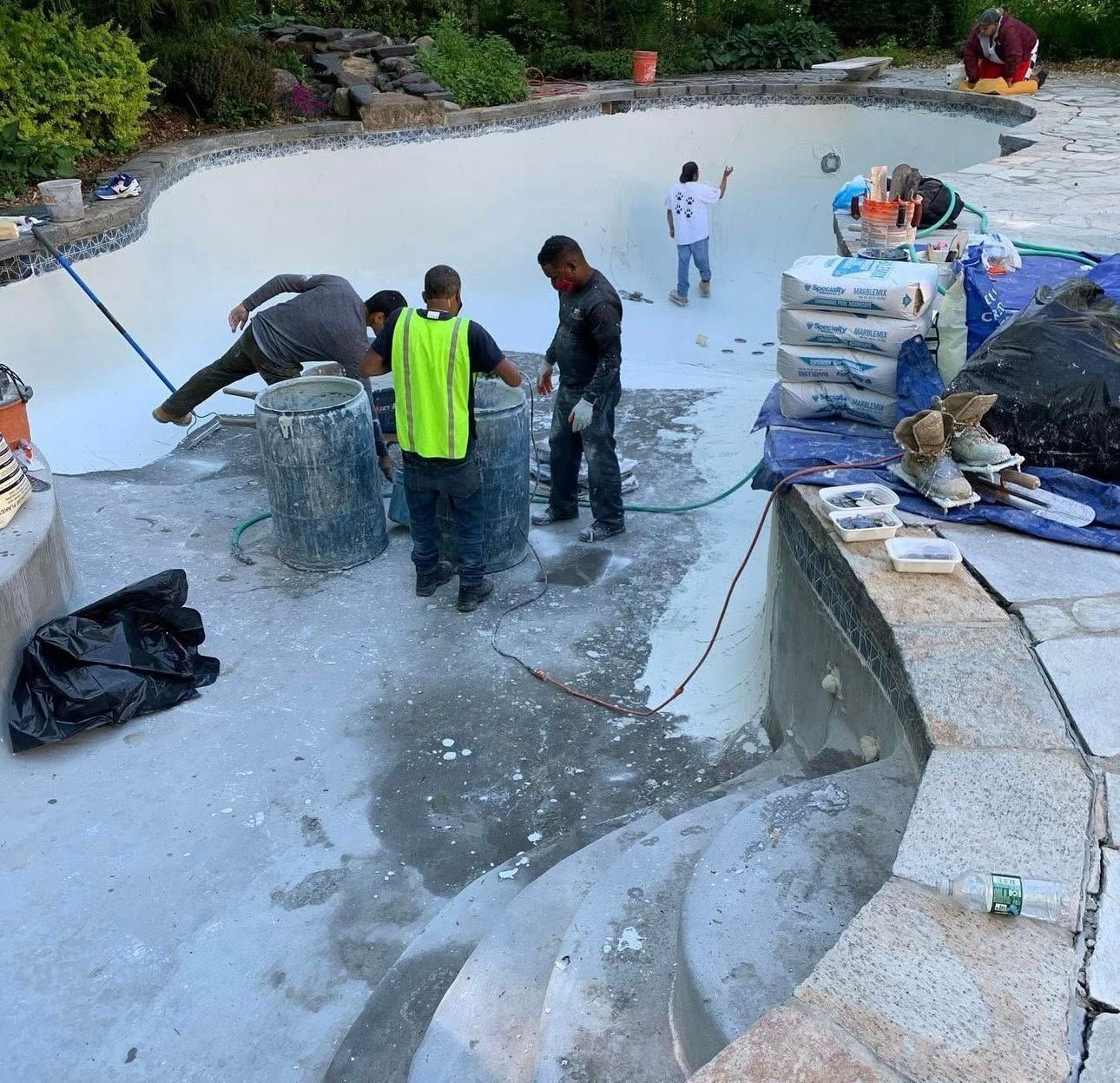 Workers resurfacing a pool with light-colored plaster. One person brushes walls, others carry buckets, scattered materials.
