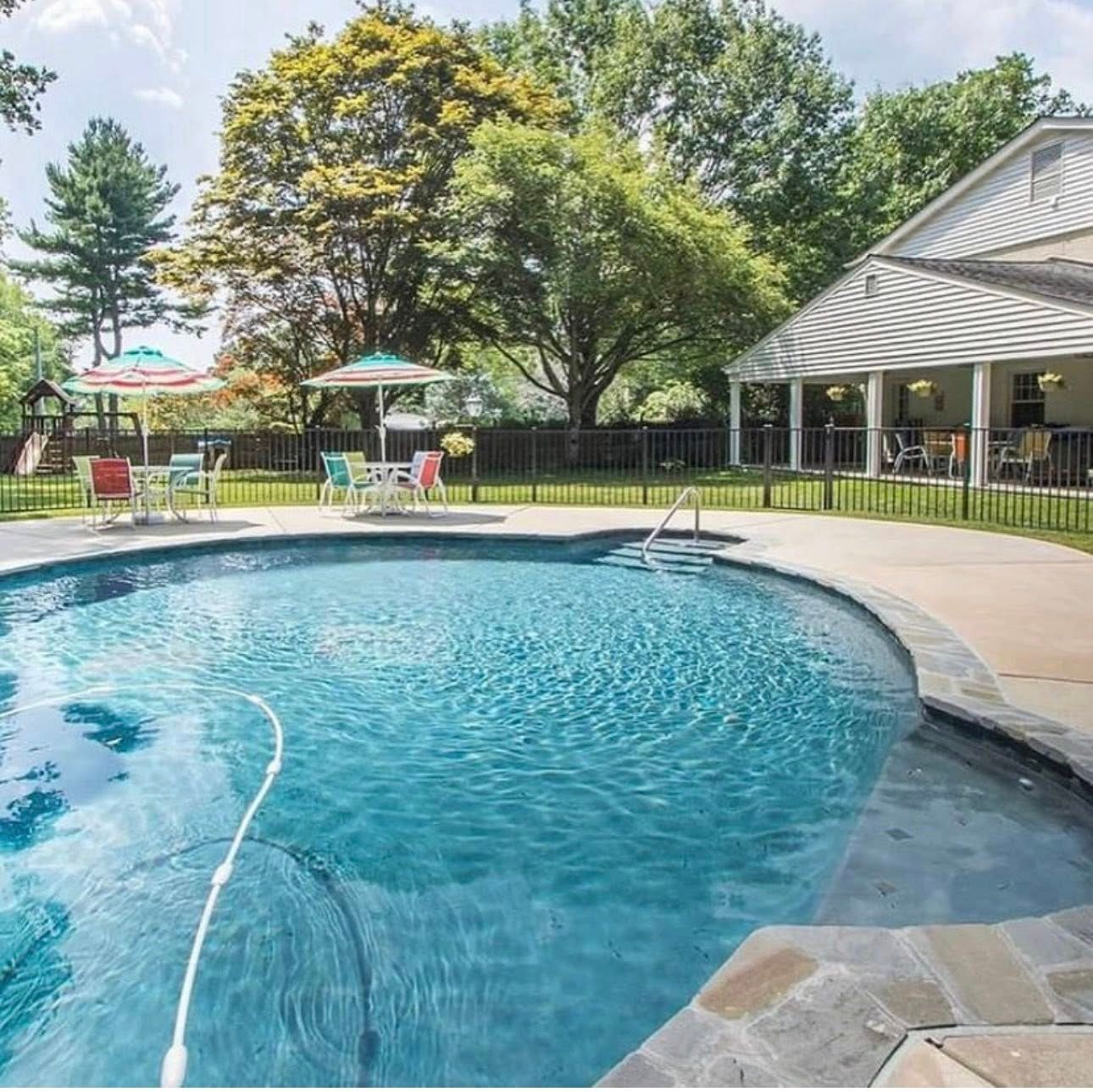 Backyard pool with umbrellas, tables, and a house with a covered porch in the background.