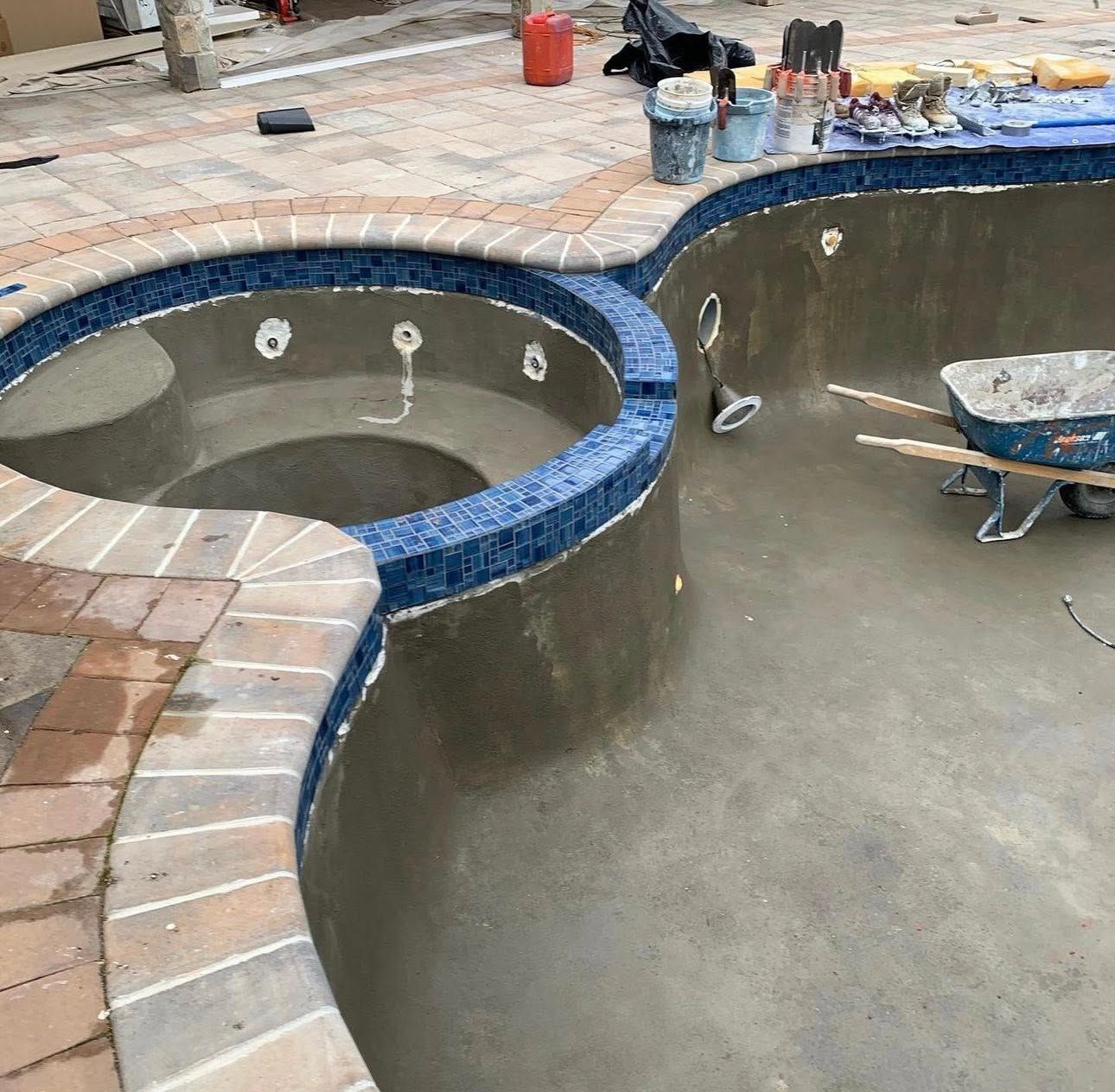 Empty pool under construction, featuring a spa with blue tile trim and brick coping.