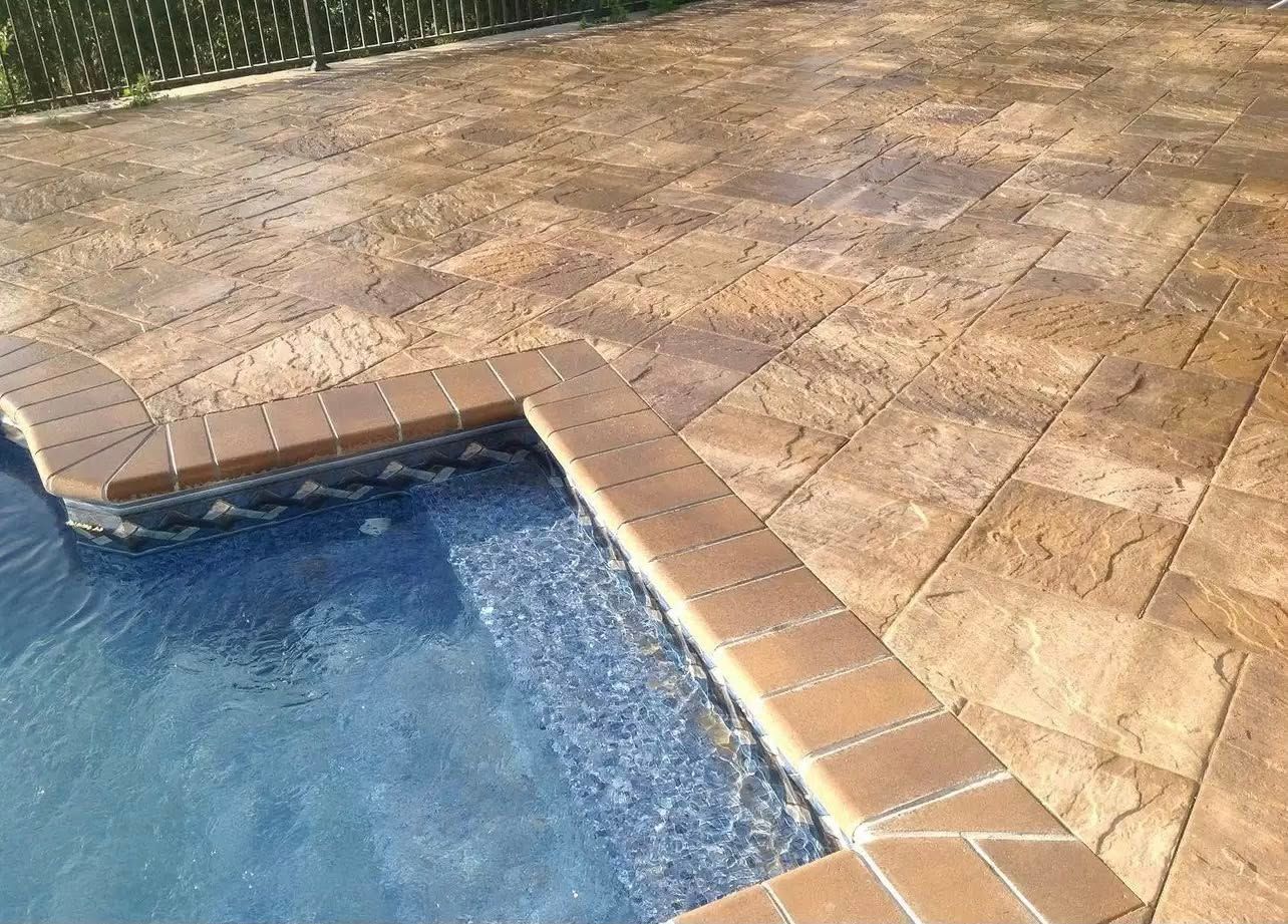 Poolside patio with brown pavers surrounding a pool with blue water.