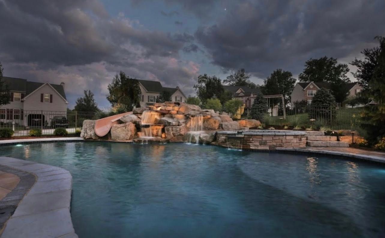 Swimming pool with a rock waterfall feature at dusk.