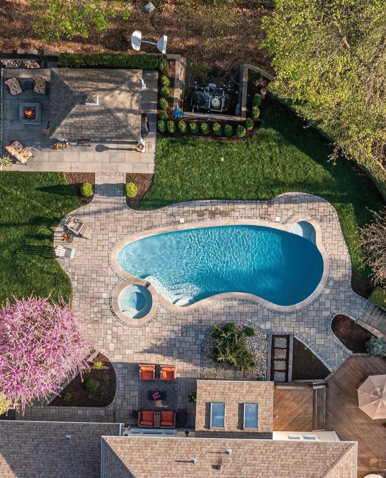 Overhead view of a backyard with a pool, patio, and lush green lawn.  A fireplace is to the left.