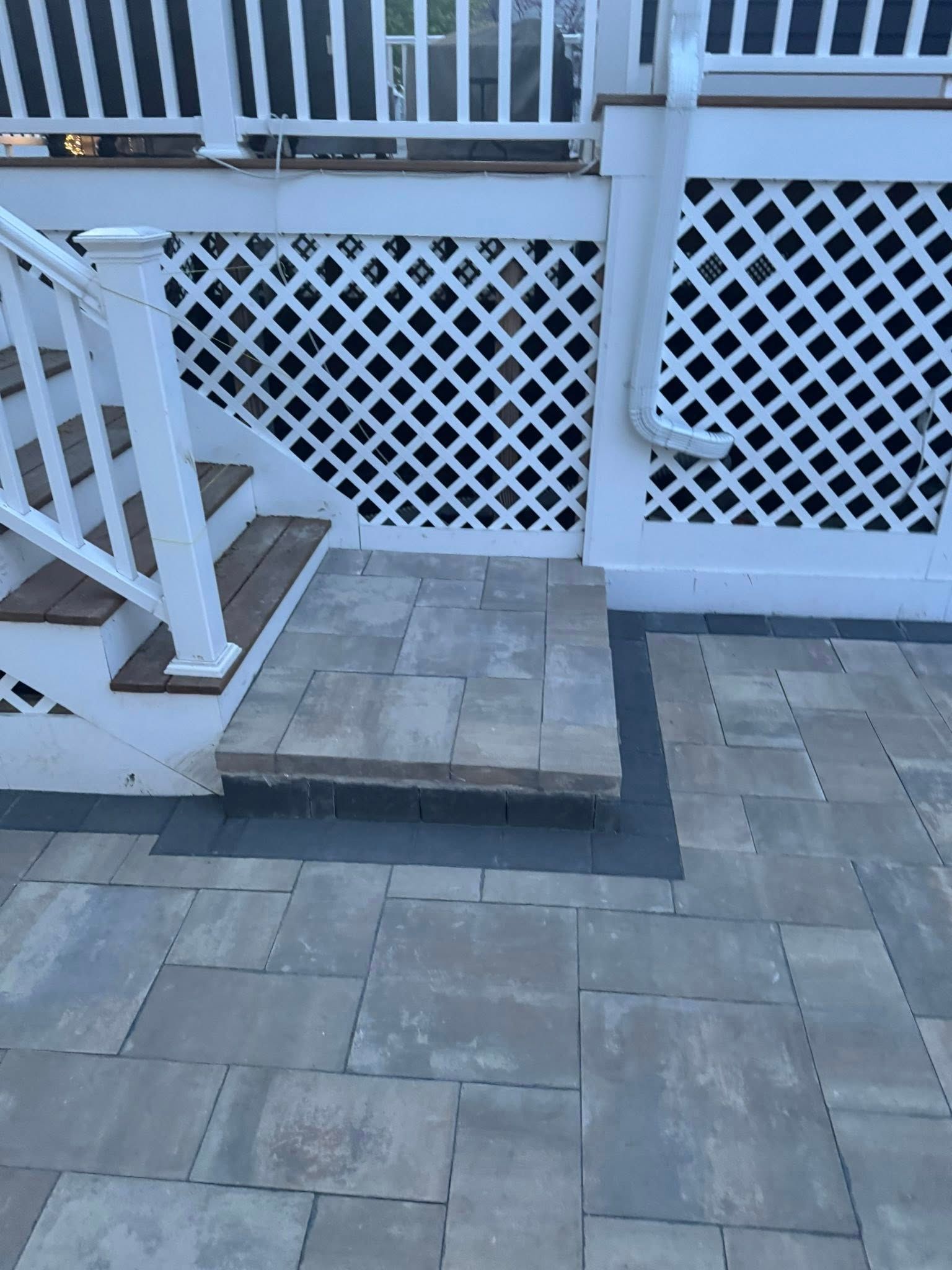 Stone patio with stairs leading to a white latticework deck with a white railing and a gutter.