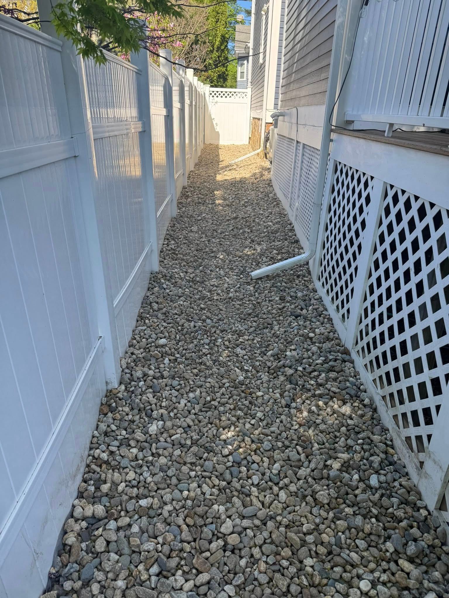 Narrow gravel-covered walkway between white fences and a house.