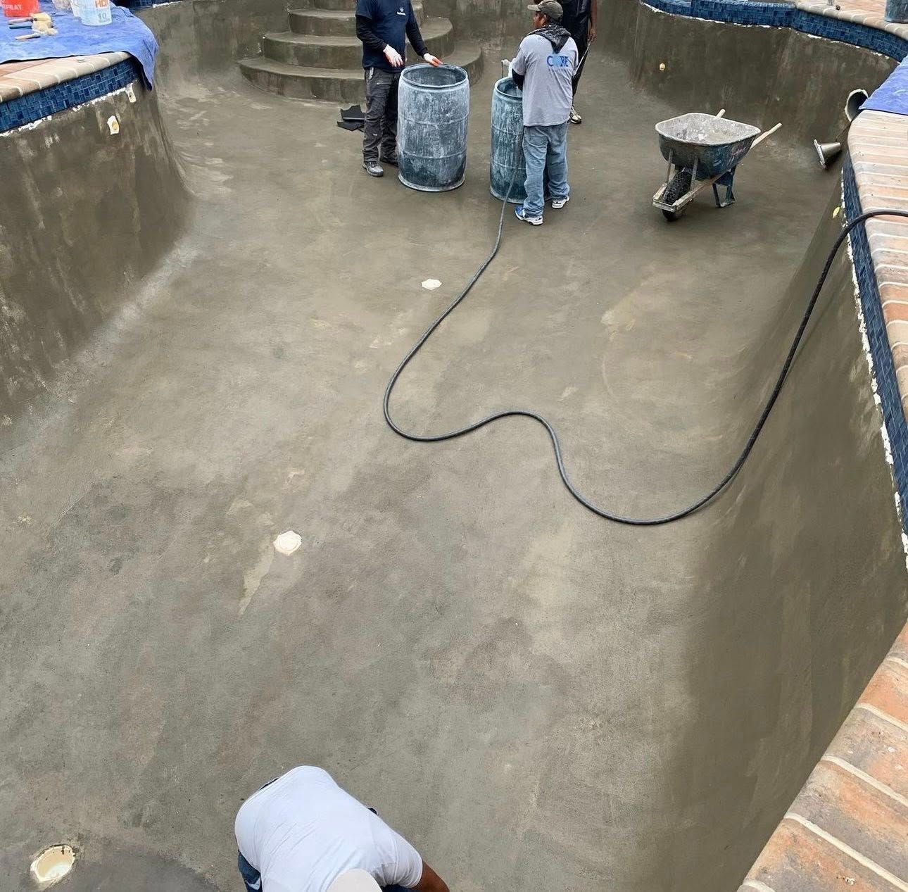 Workers resurfacing an empty swimming pool. Men in work clothes are applying a cement-like material.