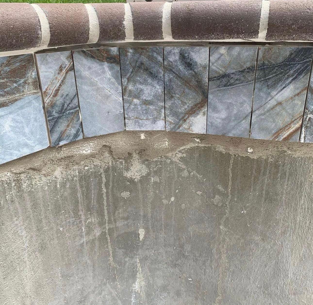 Close-up of a curved wall with stone tiles and a brick border above it, set against a concrete background.