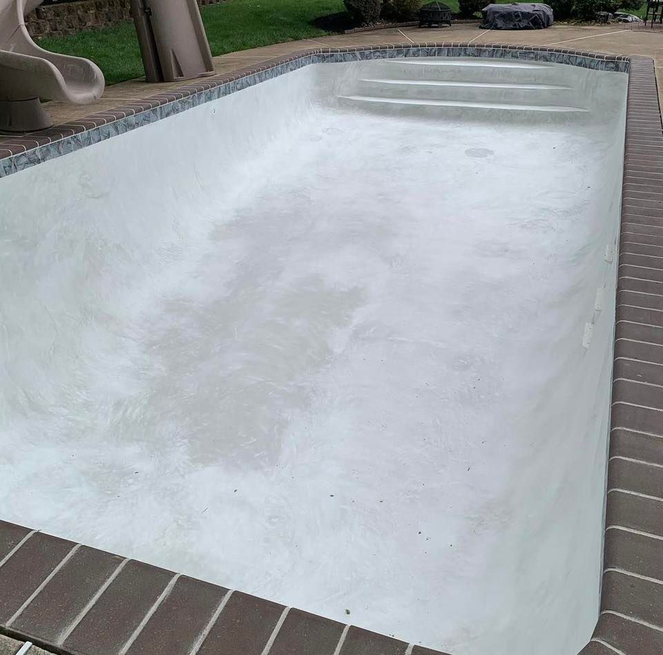 Empty rectangular swimming pool with light gray plaster, surrounded by brick.