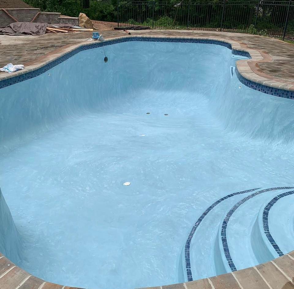 Empty, freshly painted light blue swimming pool with tiled edges and steps.
