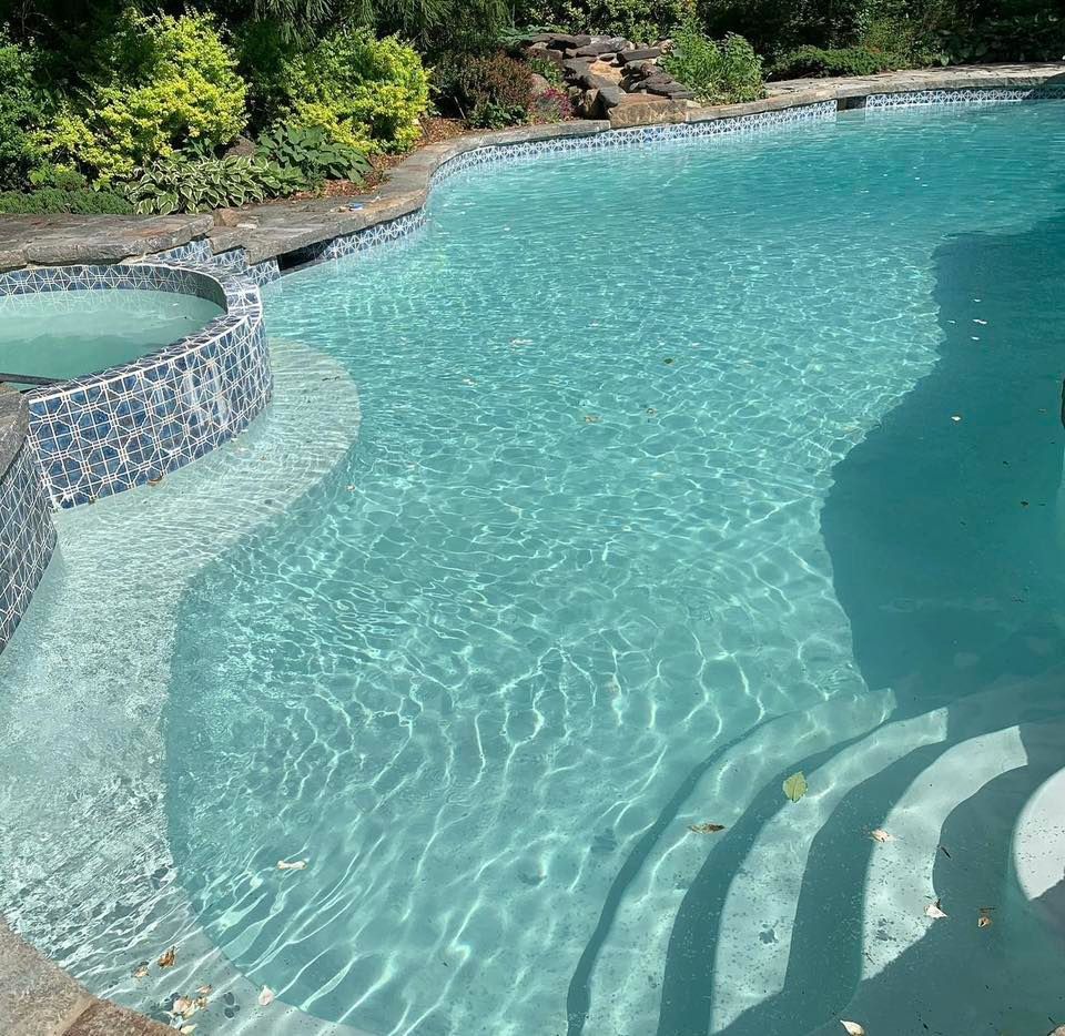 Pool with clear blue water and steps, a built-in hot tub, and landscaping.