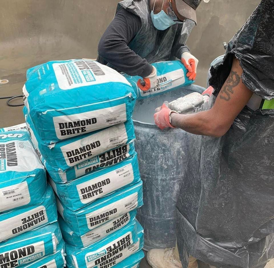 Two people wearing protective gear mixing Diamond Brite pool finish from bags into a barrel.