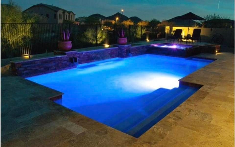 Pool with blue underwater lights, stone coping, spa, and fire feature at dusk.