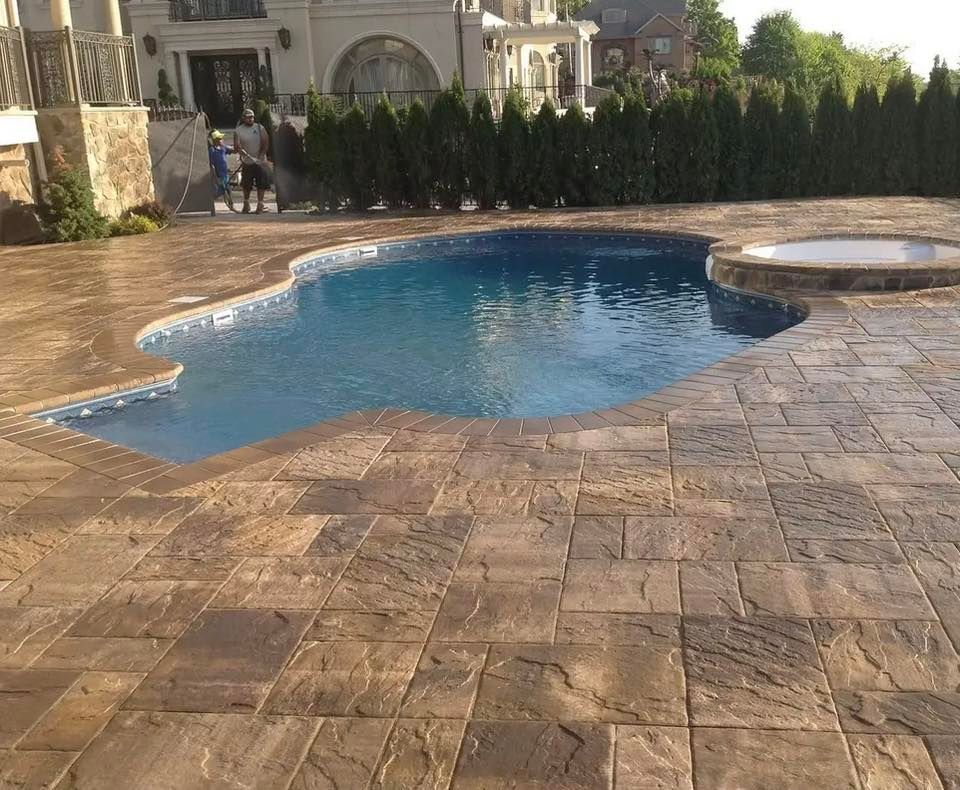 Swimming pool with stone patio, spa, and manicured landscaping in front of a large house.