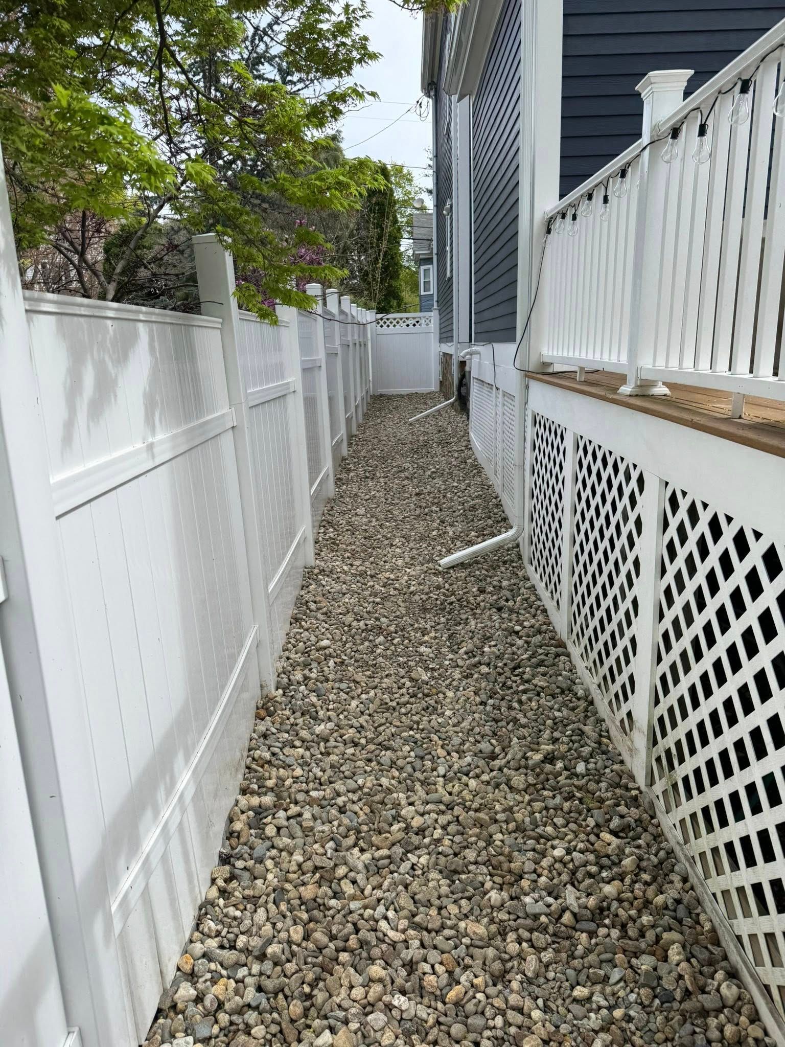 Narrow gravel walkway between a white fence and a house with lattice skirting.