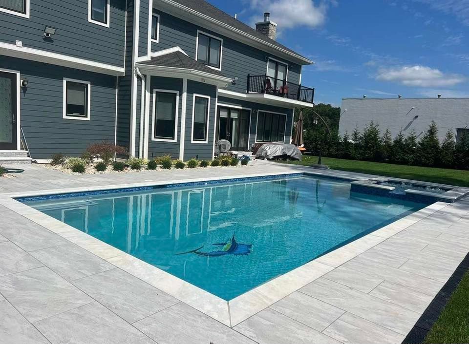 Backyard pool with light gray tile surround, blue water, and a dark gray house.