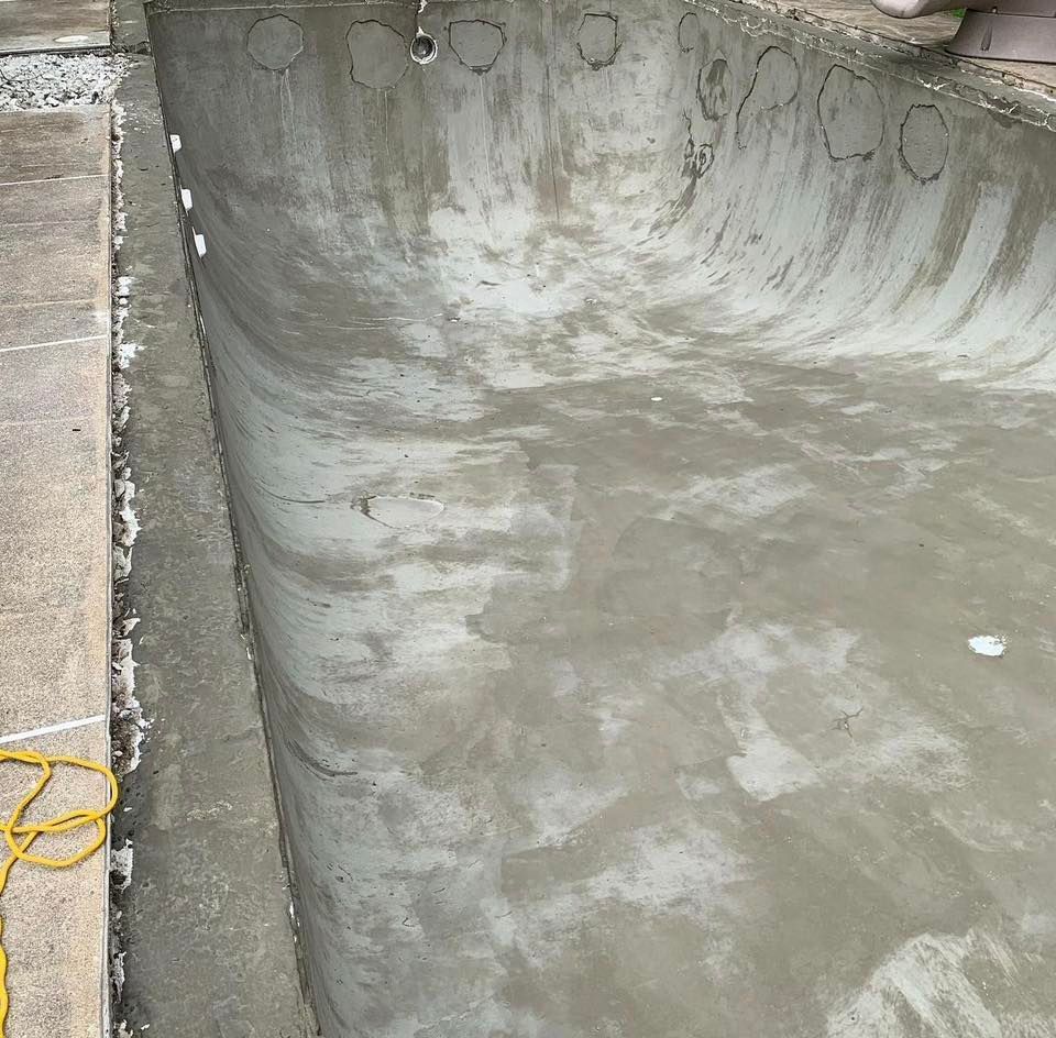 Newly plastered, empty swimming pool, grey concrete, curved edges.