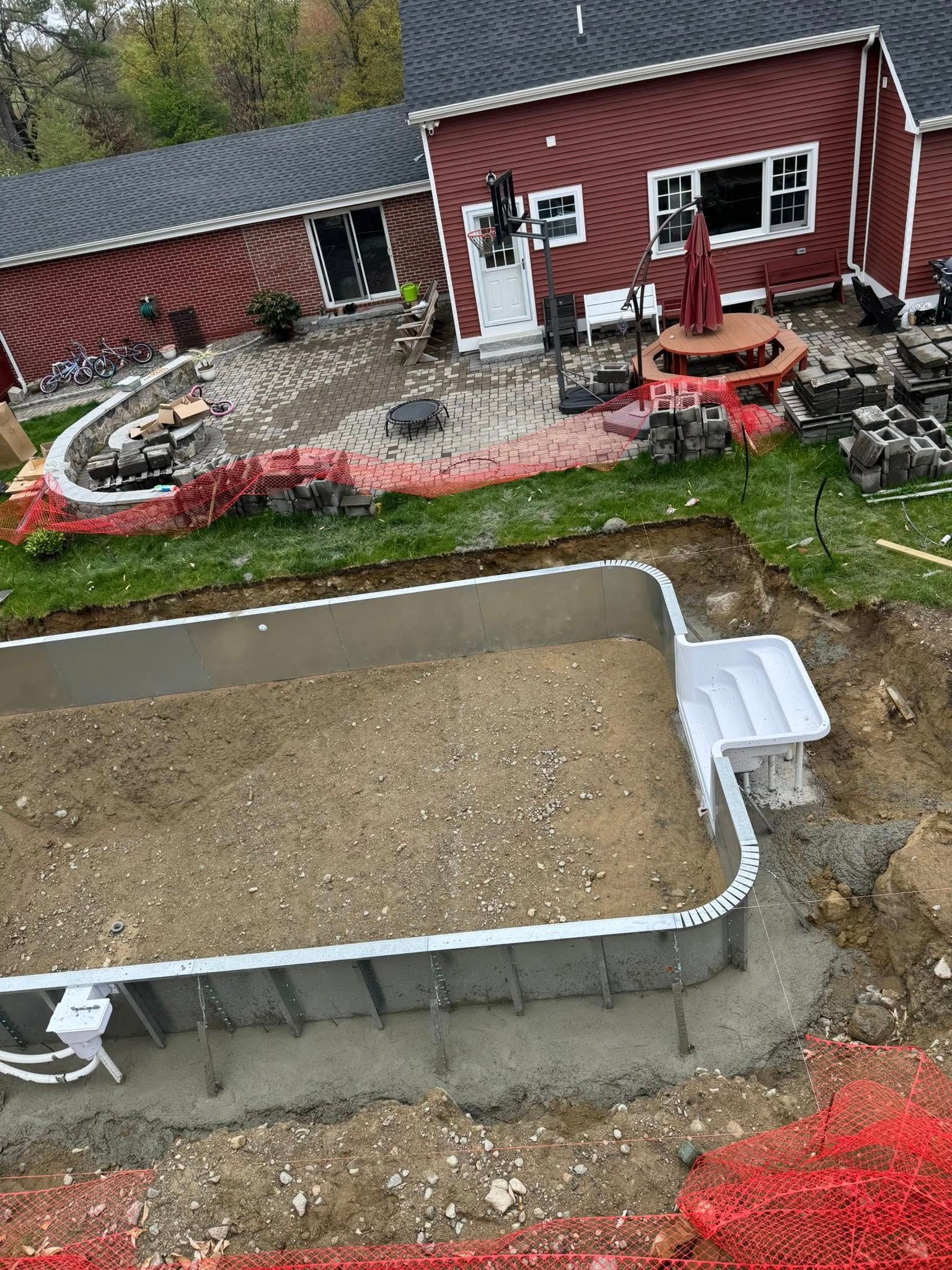 Partially built backyard swimming pool with house in the background and red safety fencing.