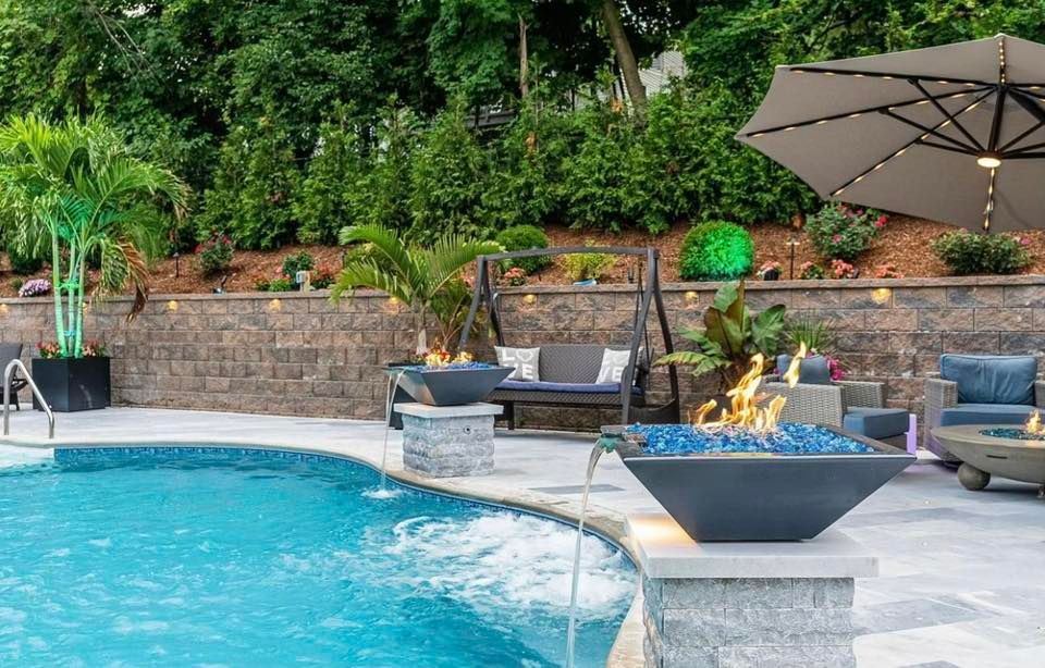 Poolside oasis with pool, fire bowls, seating, landscaping, and a large umbrella.