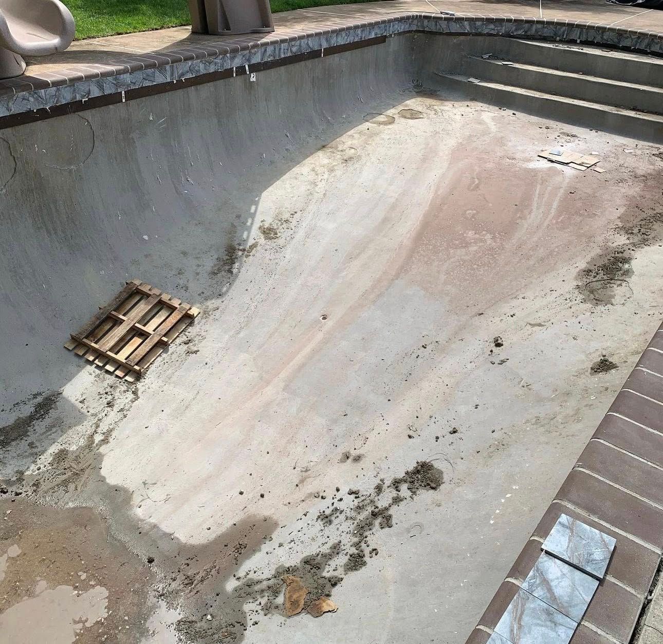 Empty concrete swimming pool, steps, and surrounding brick edging.
