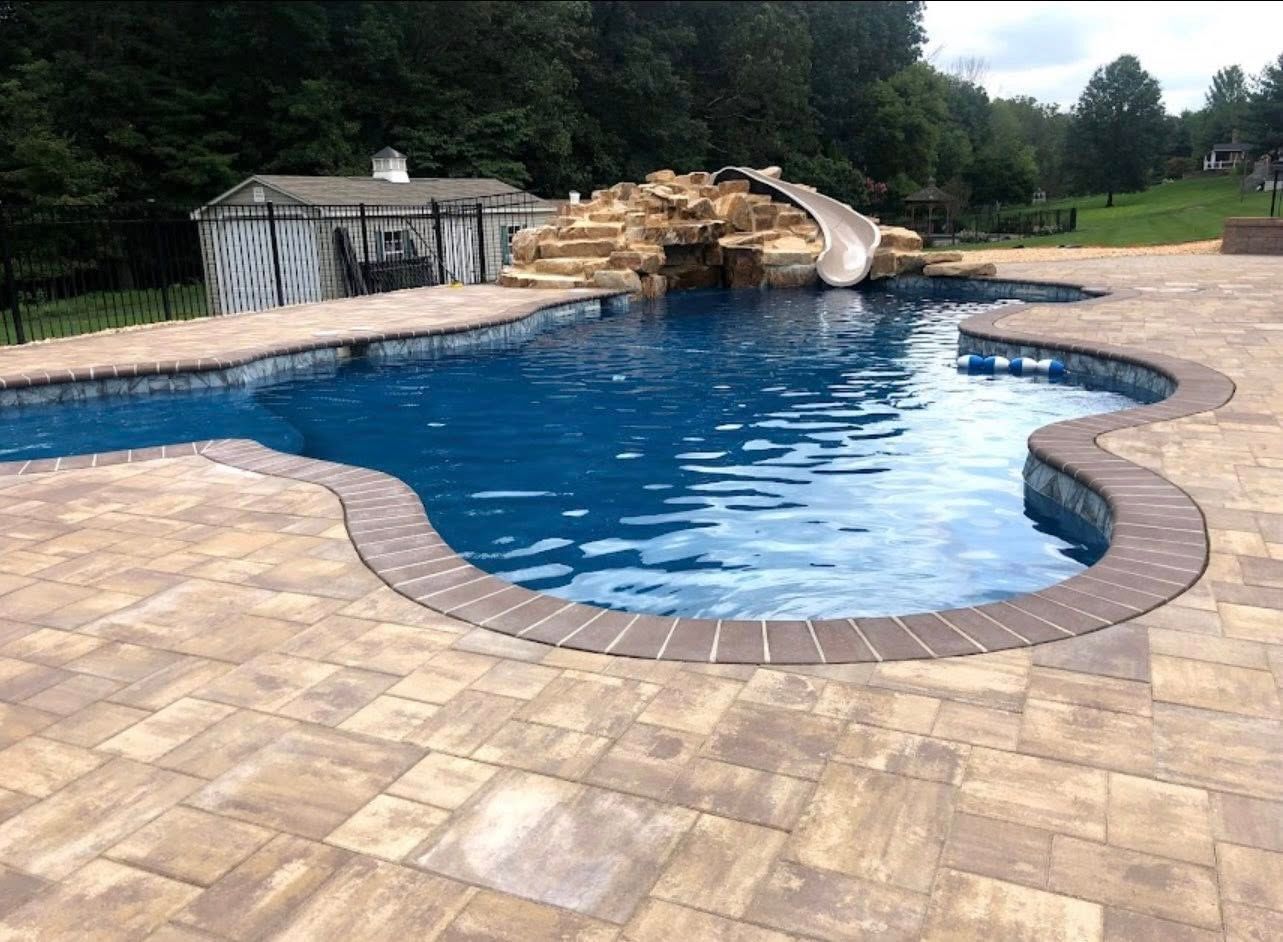 Swimming pool with a water slide and stone patio.