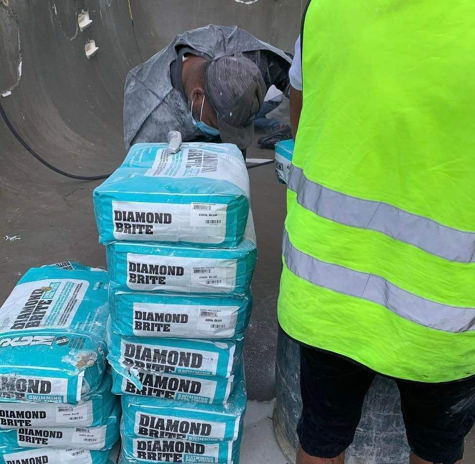 Construction worker in protective gear next to a stack of Diamond Brite cement bags.