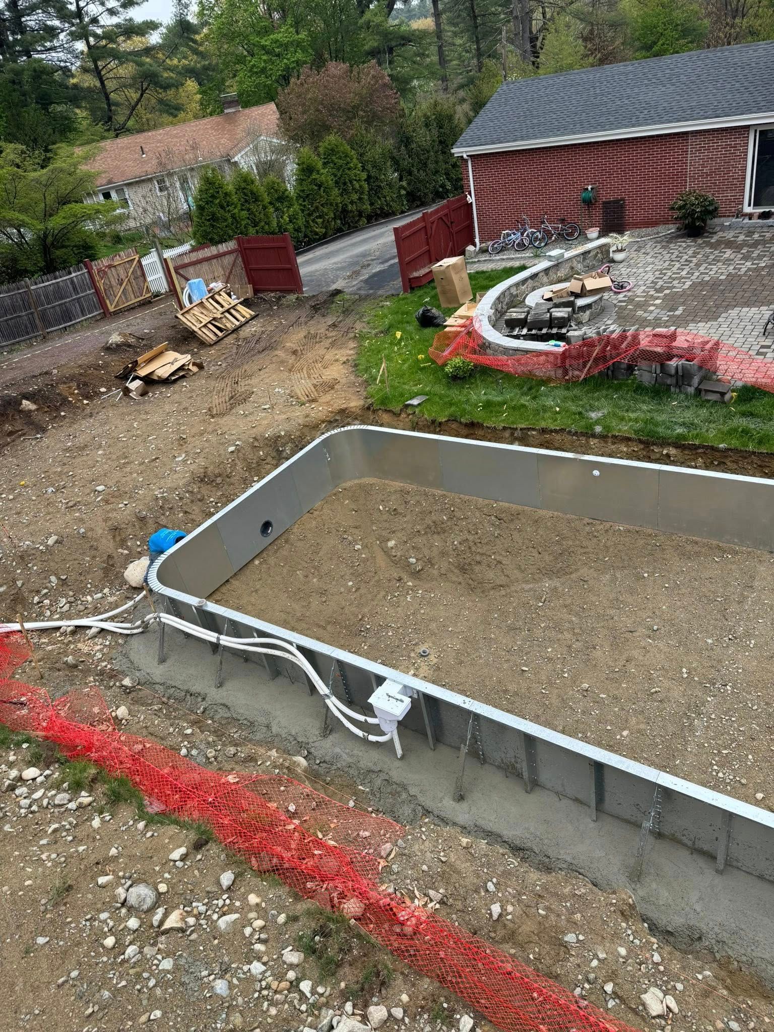 Construction site with rectangular pool frame. Red fence, dirt, and materials around the pool.