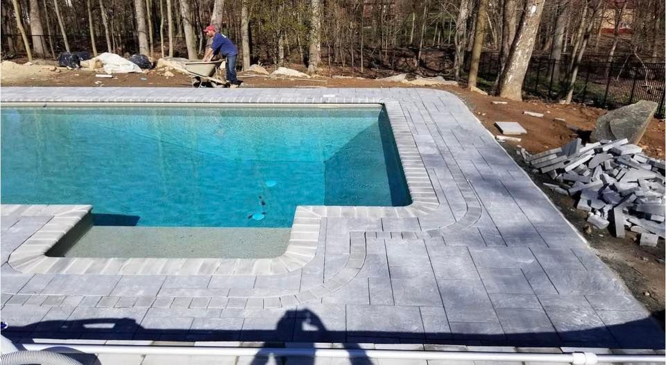 Pool with gray stone pavers being installed; a person works nearby.