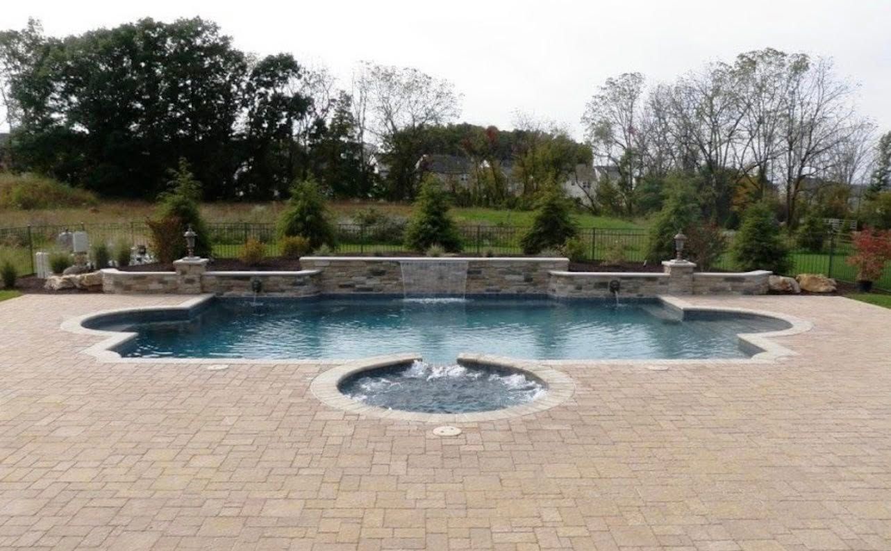 Swimming pool with cascading waterfall, surrounded by stone patio and landscaping.