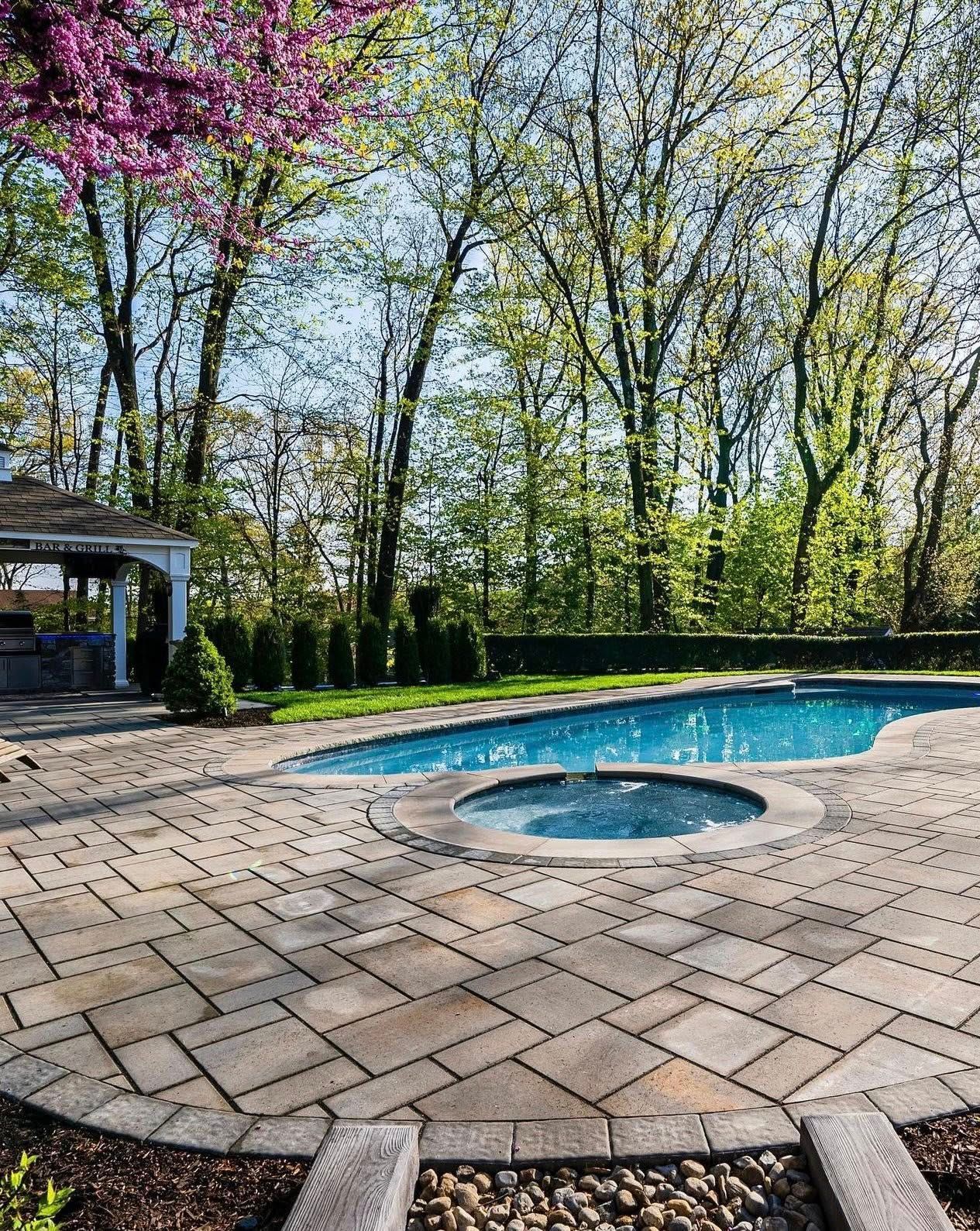 A backyard pool with stone patio, surrounded by trees and a gazebo.
